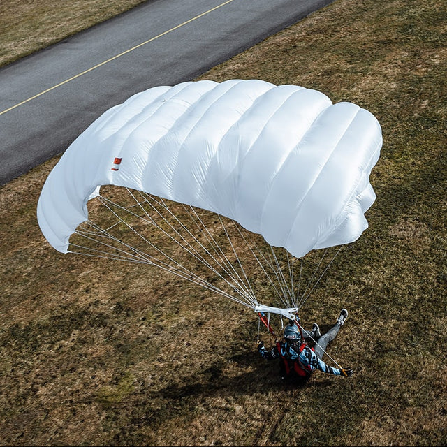 Person with a Paratec Speed Reserve Parachute landing on a grassy area near a road.